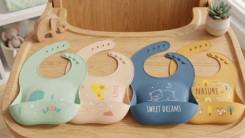 लकड़ी की मेज पर करीने से सजाए गए जानवरों की थीम वाले सिलिकॉन बेबी बिब्स का एक सेट