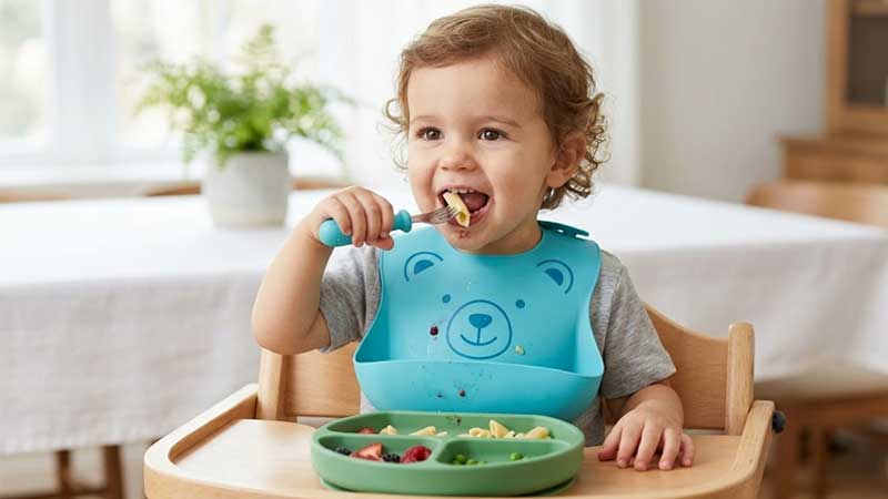 Малыш наслаждается едой в силиконовом нагруднике с изображением медведя и тарелке с разделителями.