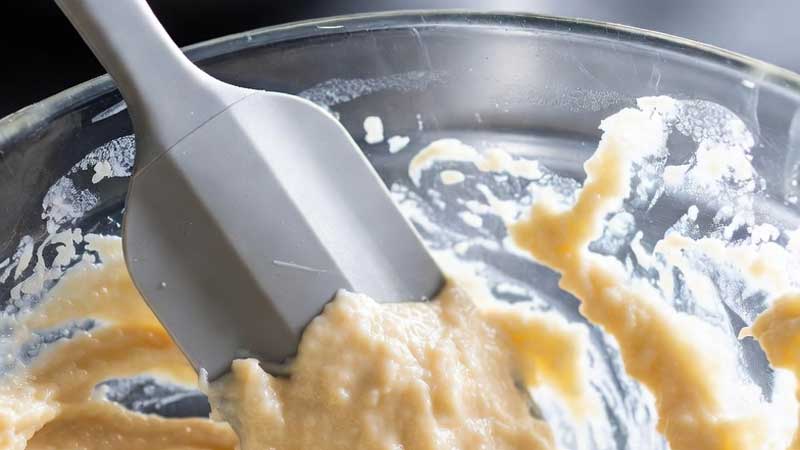 Một chiếc thìa silicon đang vét bột từ tô trộn thủy tinh.