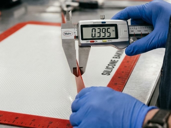 Een tester meet de dikte van een siliconen bakmat met een digitale schuifmaat voor dimensionale controle.